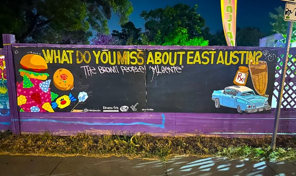 a large mural along the sidewalk in east austin asks, "what do you miss about east austin?" below that someone's painted, "the brown people! mi gente"